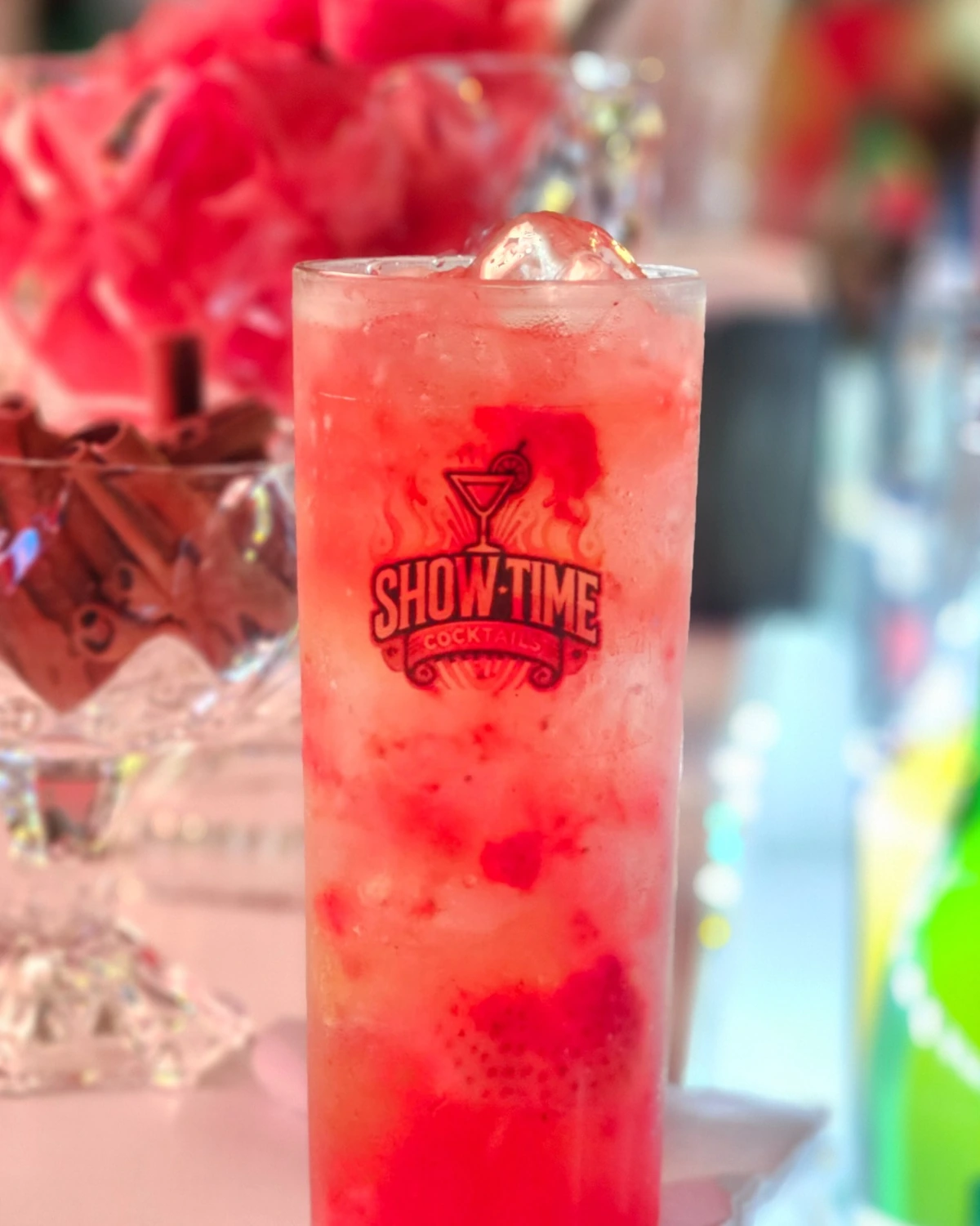 Drink vermelho servido em copo com a marca Showtime Cocktails